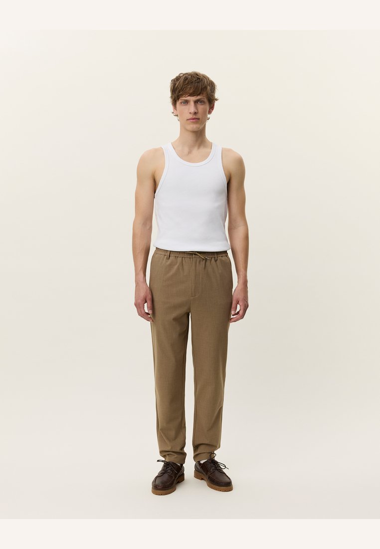 Top branco de alças, calças largas castanhas e sapatos escuros. As calças têm uma cintura elástica e um tecido texturizado. Fundo neutro.