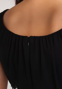 Robe noire avec un col froncé, équipée d'une fermeture éclair discrète au dos et d'un tissu doux et fluide. Aucun motif ou accent visible.