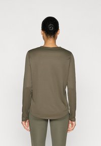 Μακρυμάνικη, τοπ σε ελαιώδη πράσινο χρώμα, κατασκευασμένο από ομαλό, ελαστικό ύφασμα. Διαθέτει στρογγυλεμένο ντεκολτέ και εφαρμοστή σχεδίαση, συνδυασμένο με κολάν στο ίδιο χρώμα.