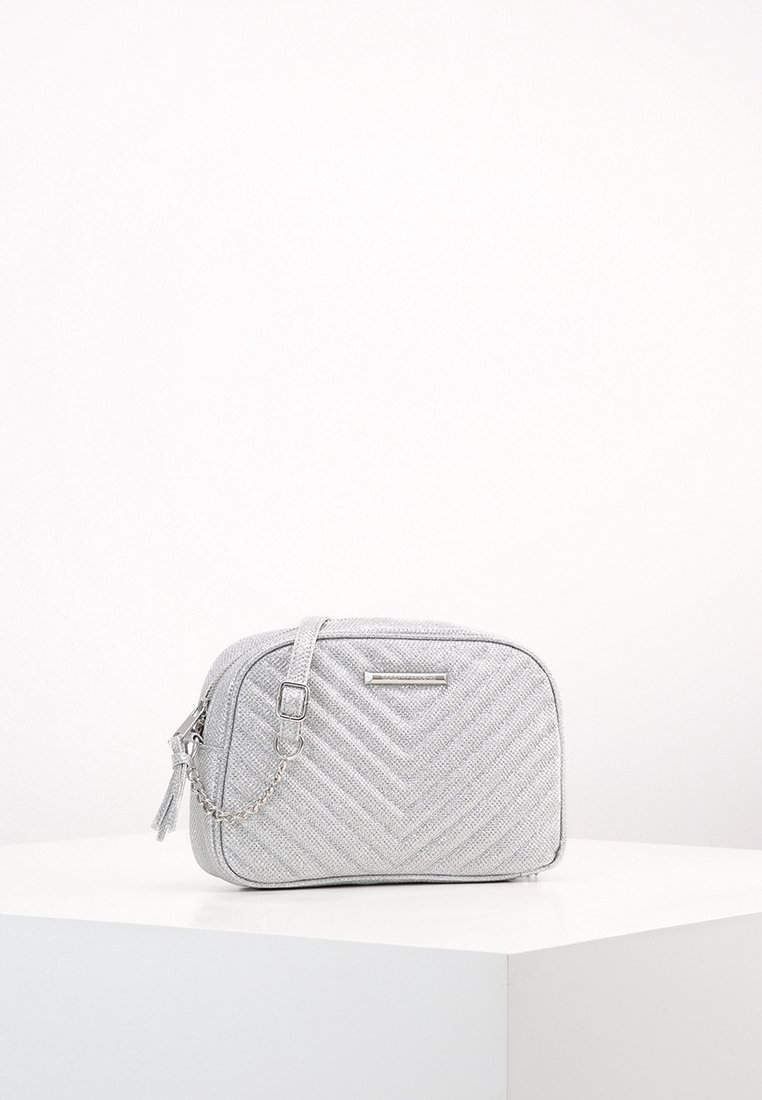 Borsa a tracolla argentata trapuntata con tracolla a catena, dotata di chiusura con zip, texture liscia e logo metallico decorativo sul davanti.