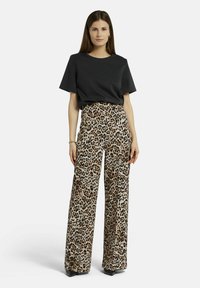 Schwarzes Kurzarmoberteil kombiniert mit weiten Hosen, die einen beigen Grundton und braune Leopardenflecken aufweisen. Das Outfit hat eine lässige Silhouette.