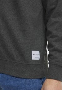 Dark grey sweatshirt made of soft fabric, featuring a ribbed hem and cuffs, with a white label on the lower left side.