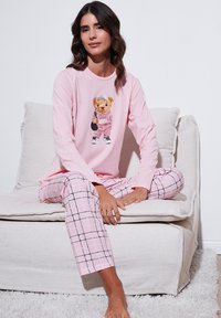 Bluza de pijama roz cu mâneci lungi, cu un grafic cu ursuleț, asortată cu pantaloni de pijama roz cu carouri. Material moale, croială lejeră și textură confortabilă.