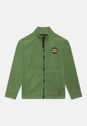 Veste polaire verte avec fermeture éclair noire intégrale, logo Ninjago sur la poitrine et petite étiquette avec logo Lego près de l'ourlet, affichée à plat sur fond blanc.