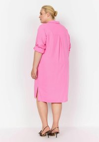 Abito rosa a maniche corte con colletto, piega sul retro e spacchi laterali; indossato con tacchi a stampa leopardata. Tessuto dalla consistenza liscia.