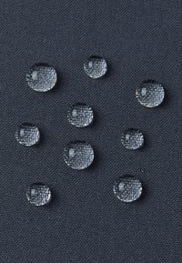 Jasne krople wody na teksturowanej ciemnej tkaninie, o różnej wielkości, pokazujące gładki, okrągły kształt na tle tkanym.