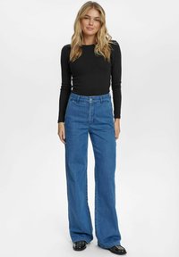 Black long-sleeve top paired with high-waisted, wide-leg blue denim jeans. The jeans feature a button closure and a classic design.