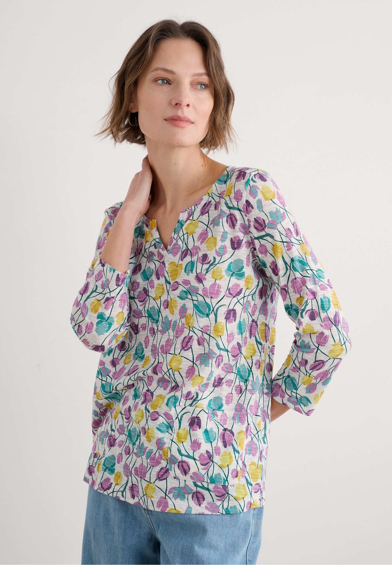 Top con motivo floreale caratterizzato da maniche corte, scollatura a V e vestibilità rilassata. I colori includono viola, giallo e turchese su uno sfondo chiaro.