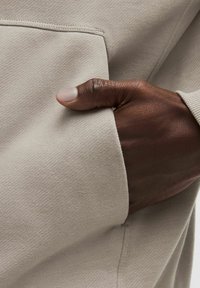 Tissu de sweat-shirt beige avec une texture subtile, comportant une poche kangourou à l'avant et une main reposant à l'intérieur de la poche.