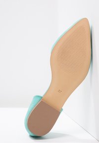 Turkos mockasko med platt sula, visar en slät tan botten och rutor för grepp. Storlek 37 angiven på sulan.