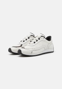 Baskets de sport blanches avec un dessus en maille texturée, accents noirs, lacets ronds, et une semelle en caoutchouc avec un motif de grip en zigzag.