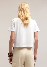 Kort vit crop T-shirt med avslappnad passform och rullade ärmar, kombinerad med beige byxor. Slät tygtextur, minimalistisk design.