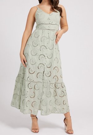 Mujer con vestido midi sin mangas de color verde claro con botones al frente y patrones de remolinos calados, combinado con sandalias de tacón alto en color nude.