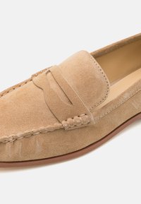 Suède loafers in licht beige met een gestikte bovenkant en een decoratieve band. Rondneus en flexibele rubberen zool. Zachte textuur met subtiele details.