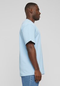 T-shirt en coton bleu clair à manches courtes et coupe décontractée, présenté sur une personne de profil contre un fond neutre.