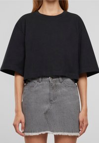 Černé zkrácené tričko s krátkými rukávy spárováno s šedou džínovou sukní s vysokým pasem, která má třepící se lem a zapínání na knoflíky.