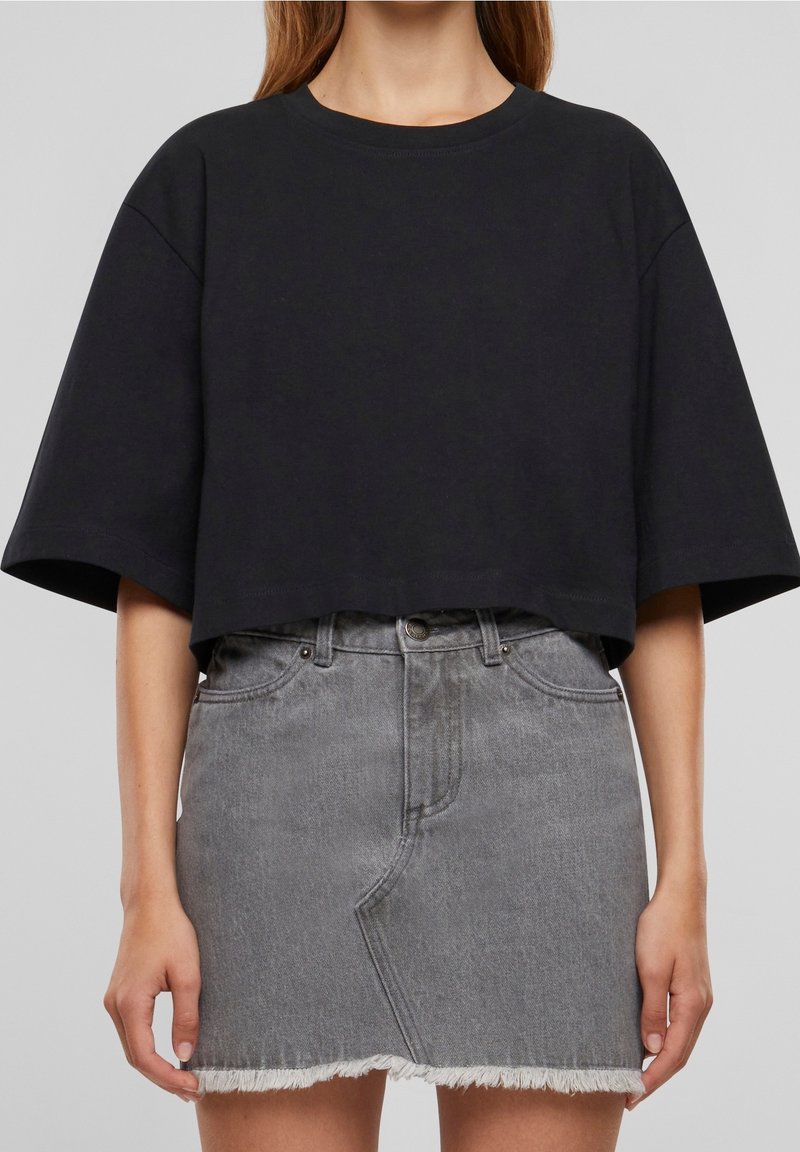 Černé zkrácené tričko s krátkými rukávy spárováno s šedou džínovou sukní s vysokým pasem, která má třepící se lem a zapínání na knoflíky.