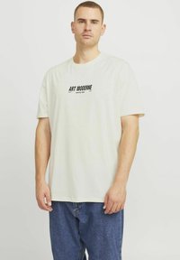 Hvid bomulds t-shirt med korte ærmer, med et sort grafisk tryk med teksten "ART MODERNE åbningsaften" på brystet. Løs pasform.