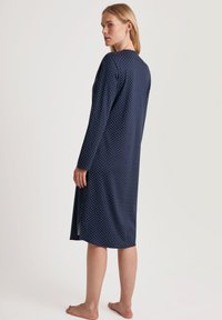 Abito lungo a maniche lunghe blu navy con pois bianchi, realizzato in tessuto morbido, presenta una vestibilità ampia e un orlo fino al ginocchio con spacco laterale.