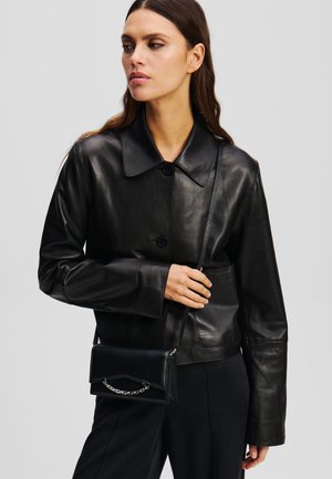 Schwarze Lederjacke mit Kragen, Knopfverschluss und langen Ärmeln. Kleine schwarze Umhängetasche mit Kettendetail.