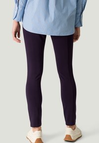 Leggings navy con una vestibilità aderente, realizzati in un materiale elastico. Abbinati a una camicia a strisce blu chiaro e scarpe da ginnastica bianche.