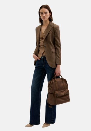 Blazer à carreaux marron, haut beige, jeans foncés évasés et ballerines beiges à bout pointu. Tenant un sac à dos marron avec une poche avant.