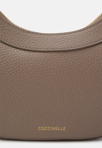 Borsa a tracolla in pelle grigia a trama ciottolosa con design curvo, dettagli della cerniera dorati e logo in rilievo vicino alla parte inferiore. Texture liscia in tutto il prodotto.