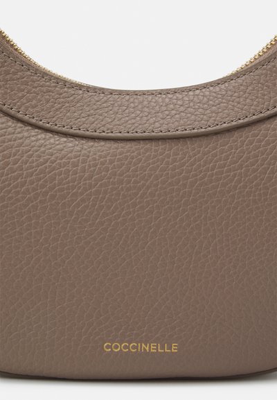 Sac à main en cuir pebble gris avec un design courbé, détail de fermeture éclair dorée et logo embossé près du bas. Texture lisse sur l'ensemble.