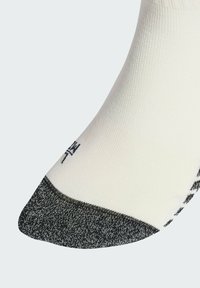 Biele ponožky s vystuženou tmavosivou špičkou a čiernym textom v blízkosti špičky, zobrazené na jednoduchom svetlom pozadí.