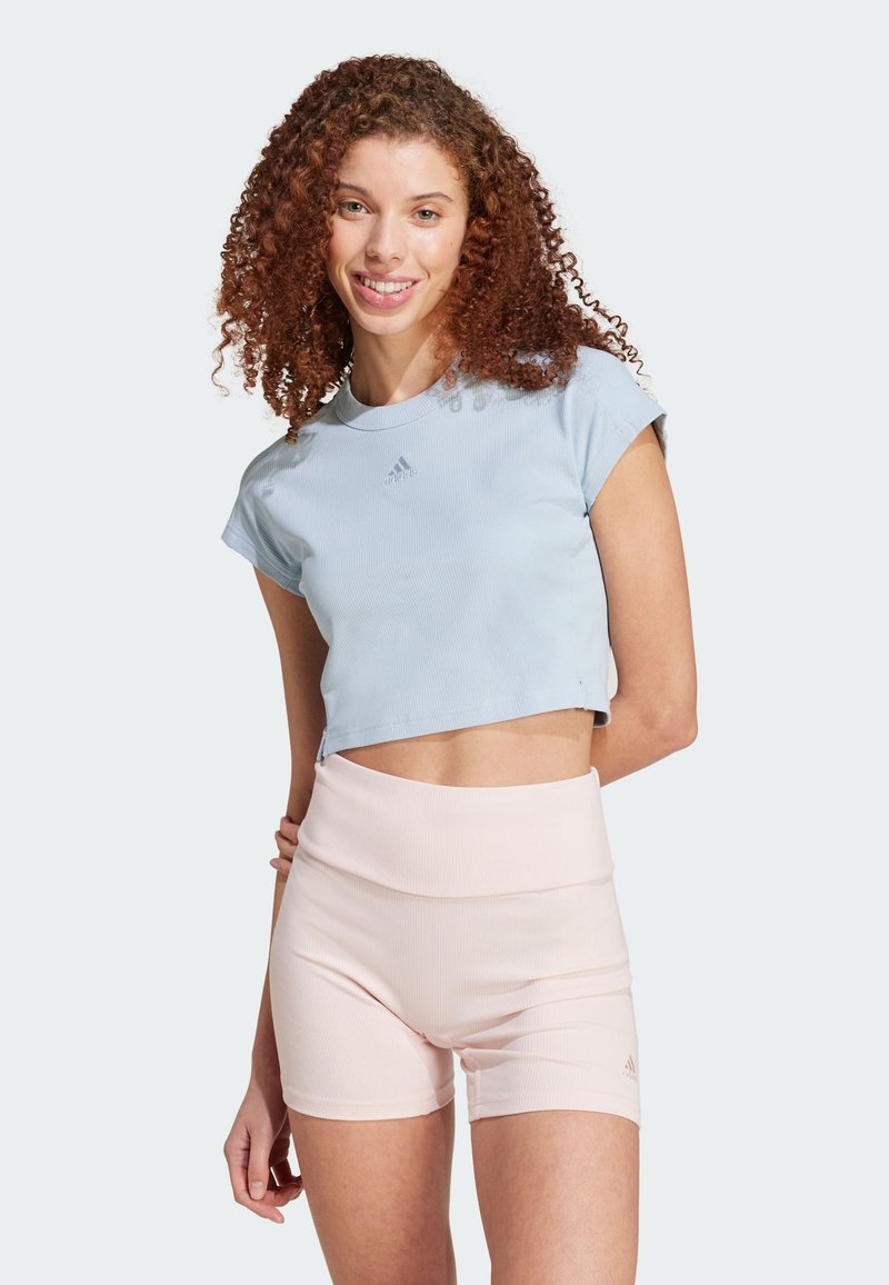 Top atletico corto azzurro chiaro con maniche corte e un logo discreto, abbinato a pantaloni corti rosa a coste a vita alta.