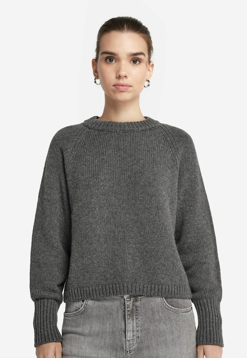 Grauer Strickpullover mit rundem Halsausschnitt, gerippten Bündchen und Saum. Hat eine lockere Passform und eine strukturierte Stoffoberfläche, kombiniert mit grauen Jeans.