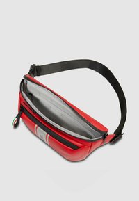 Riñonera roja hecha de material liso, con una correa negra, cremallera superior, interior gris y detalles a rayas blancas en el frente.