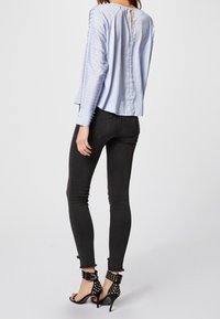 Blusa a maniche lunghe a righe blu chiaro con schiena a occhiello, abbinata a jeans neri slim-fit e sandali neri con tacco alto e borchie.