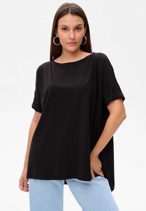 Zwart oversized t-shirt van zacht materiaal, met opgerolde korte mouwen en een ronde halslijn, gecombineerd met lichtblauwe spijkerbroek.