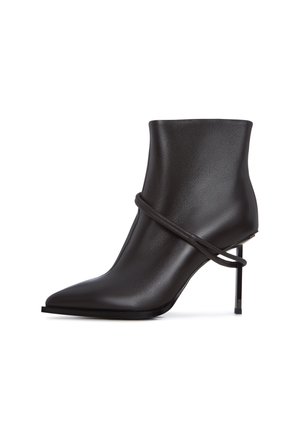 Slank sorte ankelstøvle med spids tå, indviklet designaccent og høj stiletthæl på hvid baggrund.