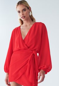 Rode chiffon wikkeljurk met een diepe V-hals, lange volumineuze mouwen en een zijstrik, met gedrapeerde details en een gelaagde rok.