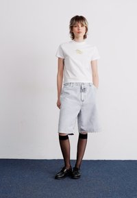 White short-sleeve T-shirt with a graphic on the chest, paired with light blue denim shorts. Black tights and black shoes complete the outfit.