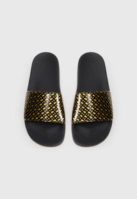 Fekete papucs sárga, fényes, geometriai mintás pánttal és texturált fekete talppal, lapos talppal és nyitott orr-résszel.