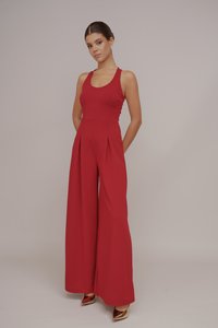 Combinaison rouge avec un corsage ajusté, un pantalon �à jambes larges et des plis. Tissu lisse et décolleté en U. Associée à des chaussures à talons hauts dorées.