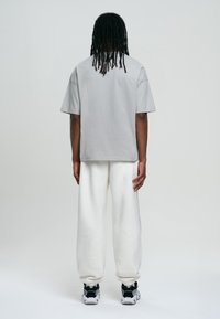 Camiseta gris de manga corta, ajuste relajado, combinada con pantalones deportivos blancos. Presenta una tela suave con cuello redondo acanalado. Zapatillas en blanco y negro.