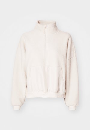 Pull en polaire beige clair avec ouverture quart-zip, col montant et poche kangourou. Manches à poignet et ourlet élastiqué ajusté. Texture douce.