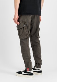 Calças de carga feitas de um tecido leve e suave numa cor verde-oliva escura. Apresenta vários bolsos laterais e punhos elásticos. Combina com ténis pretos.