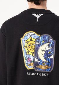 Sort sweatshirt med illustrerede sol- og månedesigns samt skyer på ryggen. Teksten "Milano Est 1978" står under grafikken.