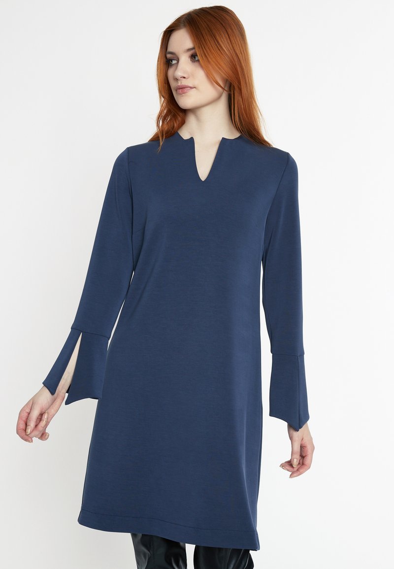 Robe bleu marine en tissu doux, avec un décolleté en V, des manches longues avec des fentes et une silhouette droite.