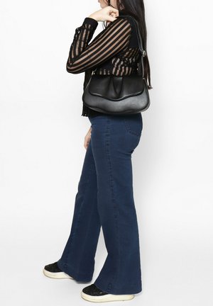 Zwarte leren handtas met een gebogen vorm, soepele textuur en subtiele naden. Gecombineerd met een doorschijnende gestreepte top en uitlopende blauwe jeans.