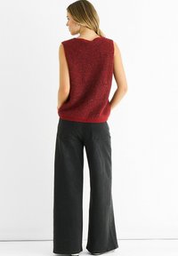 Red sleeveless knit top with a textured pattern, paired with high-waisted wide-leg black jeans featuring back pockets and a faded finish.