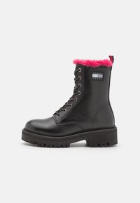 Bota de combate negra con cordones, suela gruesa, con borde de piel de color rosa y parche del logo de Tommy Jeans en el costado.