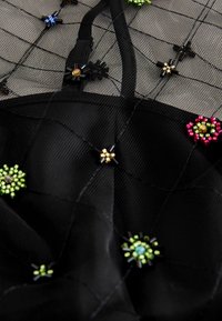 Schwarzer Netzstoff mit floralem Perlenbesatz in verschiedenen Farben. Verfügt über dünne Träger und eine strukturierte Oberfläche mit gitterartigen Mustern.