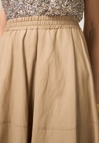 Beige midi-rok van lichte, gestructureerde stof met een elastische tailleband, voorzien van zachte plooien en contrasterende stikdetails.