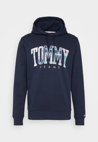 Sudadera azul marino con cordón, que presenta un logotipo gráfico "TOMMY JEANS" en patrones coloridos. Textura suave con puños y dobladillo acanalados.